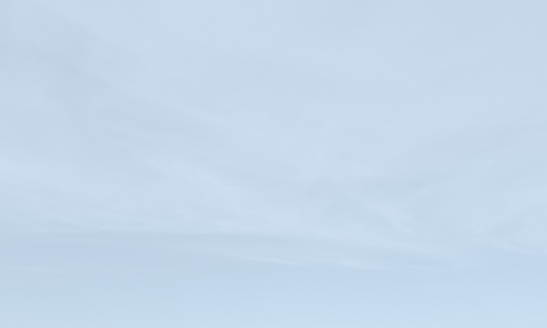 Pale blue sky with thin streaks of high cloud, seen from far above the hills