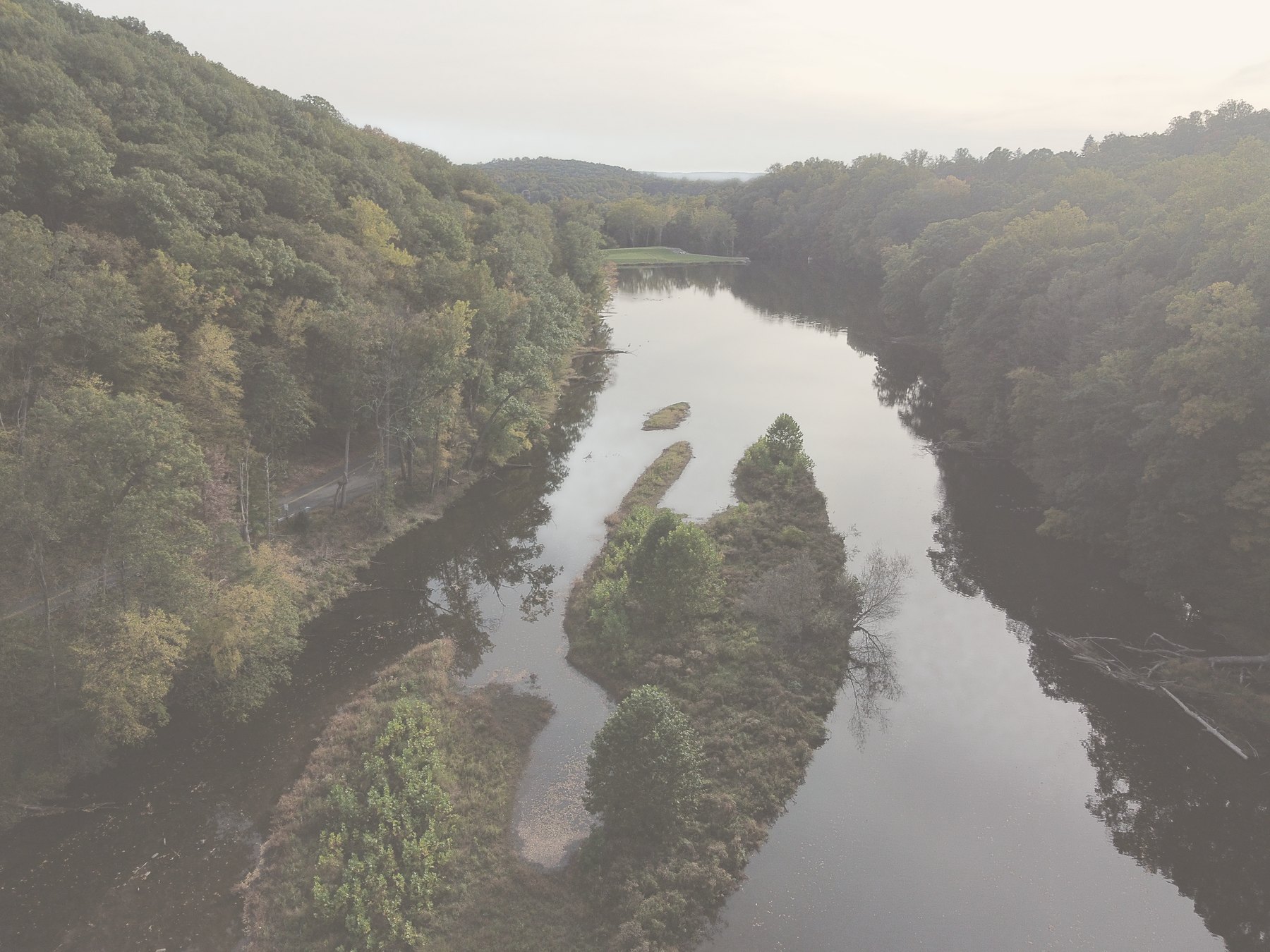 A small wooded island in the middle of a calm river, with mirror reflections
